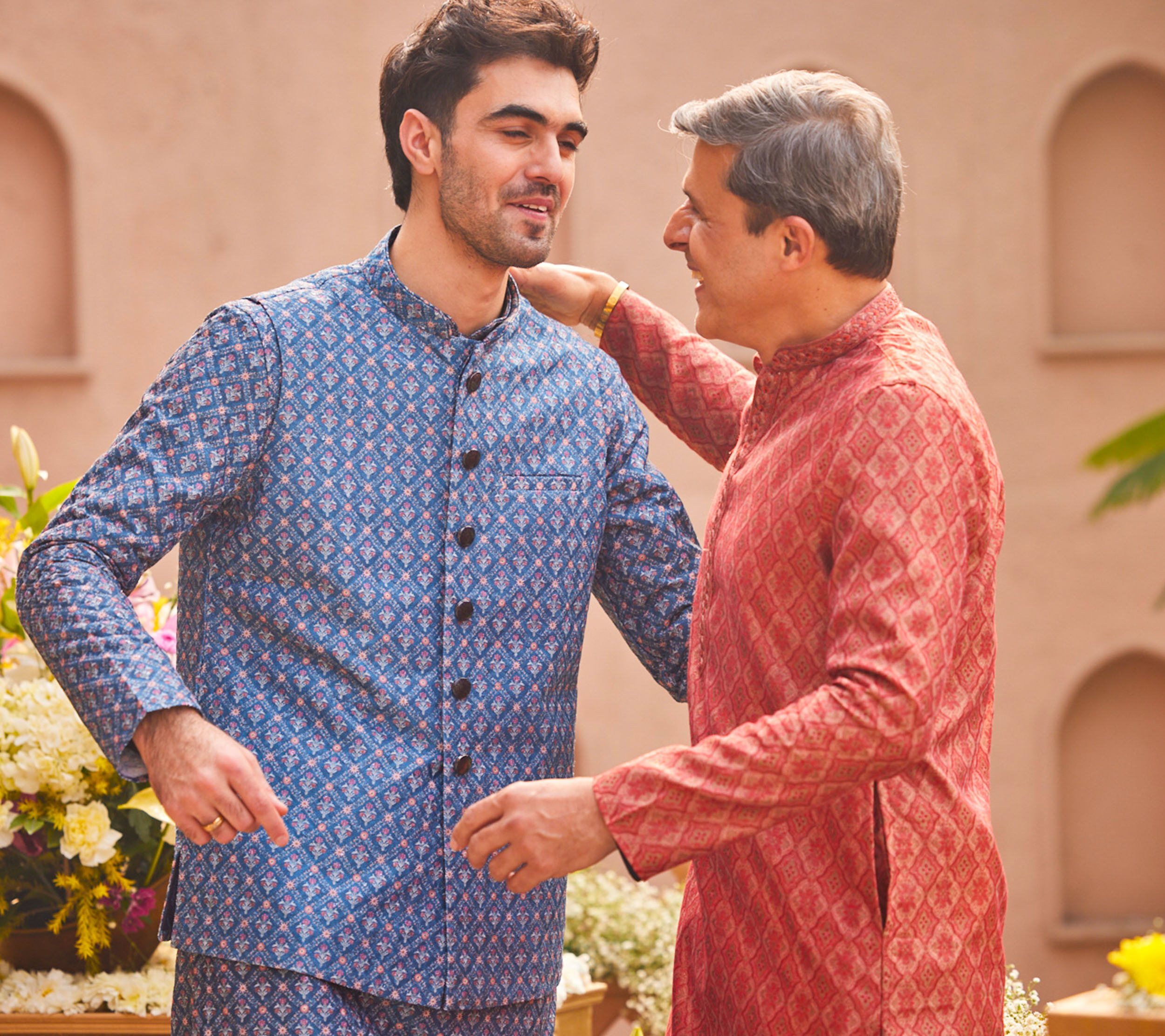 Father and son sharing a joyful moment in matching Eid outfits, wearing coordinated blue and red patterned kurtas.